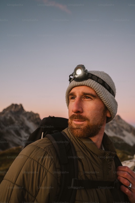 Hiker wearing a headlamp at sunset with mountain peaks in the background