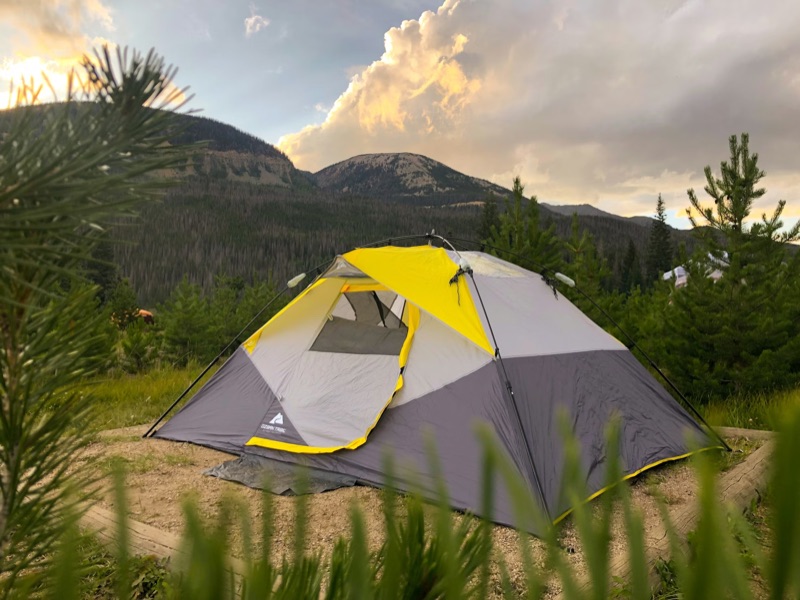 Yellow and gray dome tent pitched in a mountain clearing at golden hour